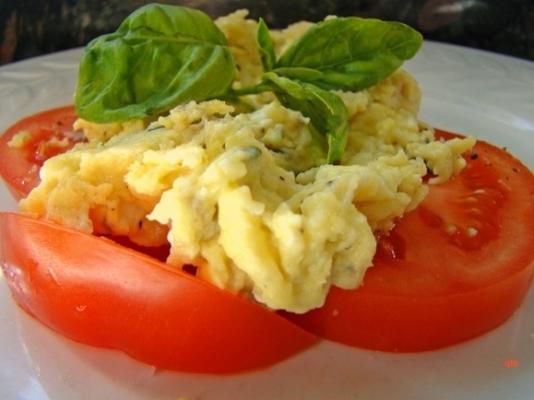 œufs brouillés sur tomates fraîches tranchées et basilic